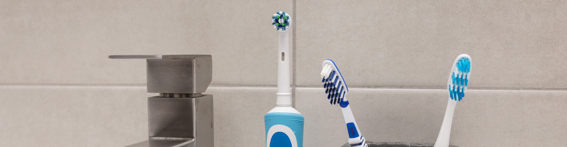 Electric and manual toothbrushes on sink beside faucet.